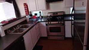 A compact kitchen with white cabinets, a stainless steel refrigerator, a stove, and a sink.