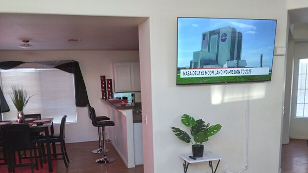 A modern living room with a dining area, a kitchen, and a TV displaying a NASA message.