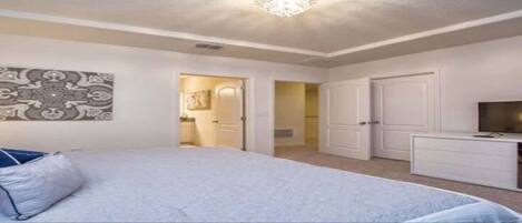 A bedroom with a bed, a TV, a wardrobe, and a door leading to a bathroom.
