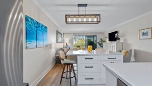 Cocina moderna con isla central, armarios blancos y una lámpara colgante.