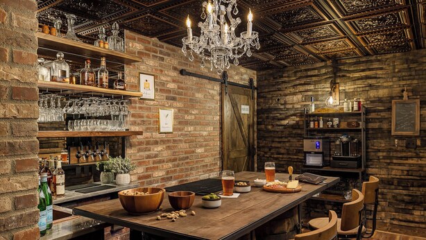 Eine Bar mit Holzboden, Regalen voller Flaschen und Gläser, einer Kristallleuchtre und einem Schild, das einen privaten Bereich kennzeichnet.
