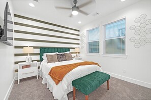 Un dormitorio moderno con cama, mesitas de noche, un banco, ventilador de techo y ventana con persianas.