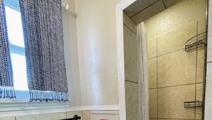 Een badkamer met toilet, douche en raam met gordijnen met een patroon.