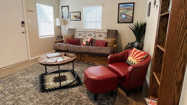 Een woonkamer met een bank, een rode fauteuil, een salontafel en een vloerkleed.