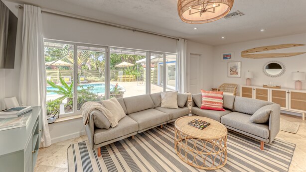 A spacious living room with a large sofa, a round coffee table, and a view of a pool outside. - Newly Renovated Beach House w Heated Pool, 4 BR, 3 BA (Fort Lauderdale)