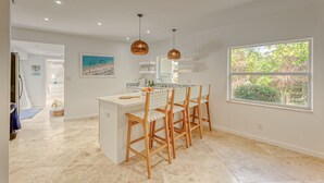 A modern kitchen with a central island, wooden chairs, pendant lighting, and a large window. - Newly Renovated Beach House w Heated Pool, 4 BR, 3 BA (Fort Lauderdale)