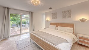 A bedroom with a large bed, a nightstand, a chandelier, and a view of the outdoors. - Newly Renovated Beach House w Heated Pool, 4 BR, 3 BA (Fort Lauderdale)