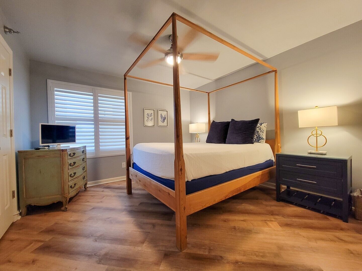 A four-poster bed with a wooden frame, a television on a dresser, and a lamp on a nightstand.