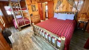 A wooden cabin-style bedroom with a bunk bed, a wooden dresser, and a bed with a checkered bedspread. - Cozy Cabin with Lake Views - Rustic Getaway (Indian Lake)