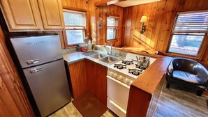 A compact kitchen with wooden cabinets, a refrigerator, a stove, and a sink. - Cozy Cabin with Lake Views - Rustic Getaway (Indian Lake)