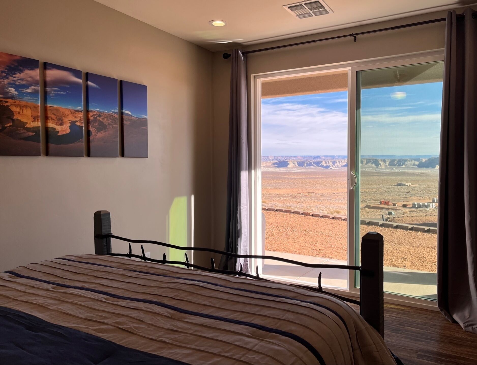 Un dormitorio con una cama grande, vista a un paisaje desértico a través de una puerta corrediza de vidrio, y tres cuadros en la pared.