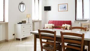 A dining area with a white table, wooden chairs, a red sofa, and a television on the wall.