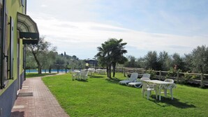 A grassy outdoor area with white lounge chairs and a table, a brick pathway, and a view of a body of water in the background.