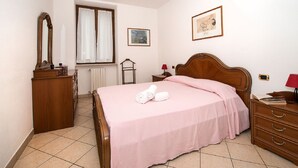 A bedroom with a wooden bed, a dresser, a mirror, a window with curtains, a bedside table with a lamp, and a framed picture on the wall.