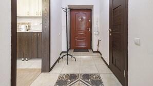 Um corredor com porta de madeira, um cabideiro de metal e chão de azulejos.