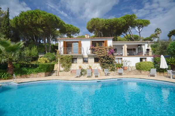A two-story house with a swimming pool, surrounded by lush greenery and trees.