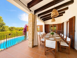 A terrace with a pool, dining table, chairs, and a view of the landscape.