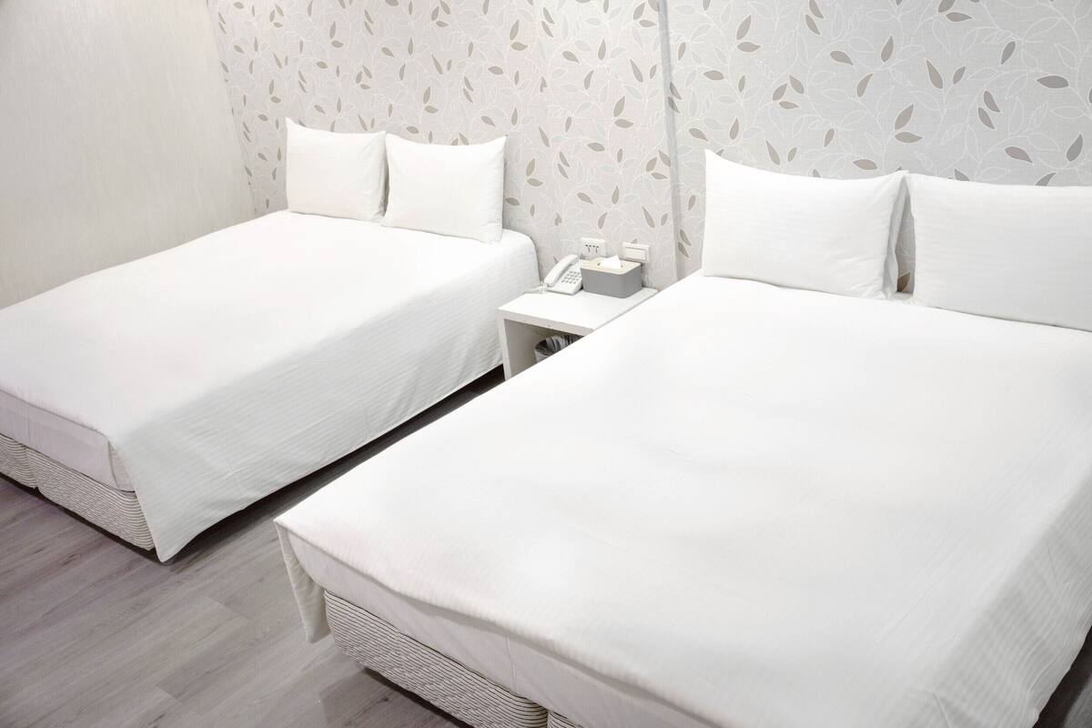 A hotel room with two single beds, a small bedside table with a phone, and a wall with a leaf pattern.