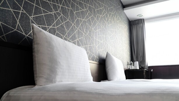 A modern hotel room with a large bed, a geometric-patterned wall, a nightstand with a lamp, and a window with curtains. - Star Ximen (Taipei)
