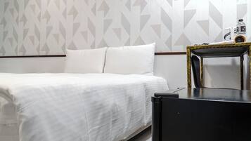 A neatly made bed with white linens in a room with geometric patterned wallpaper.