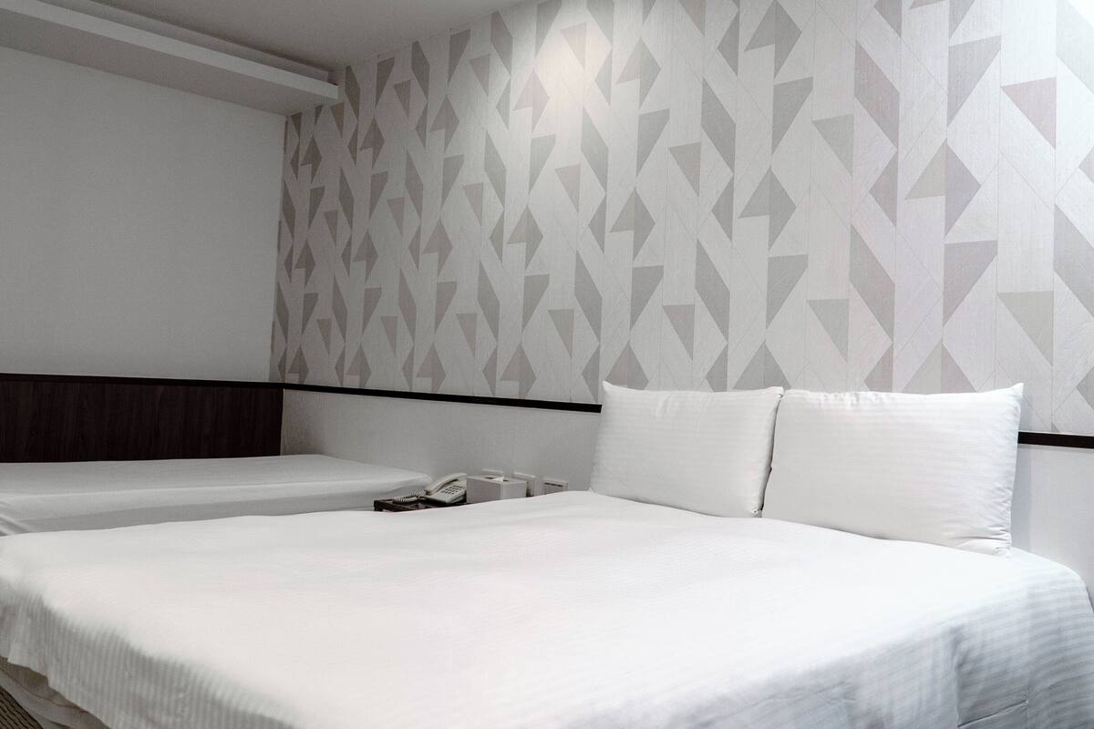 A hotel room with two beds, a wooden headboard, a patterned wall, and a telephone on the nightstand.