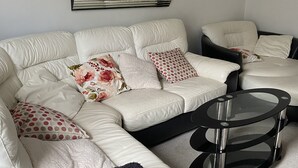 Een moderne woonkamer met een hoekbank, een glazen salontafel en een decoratieve spiegel aan de muur.