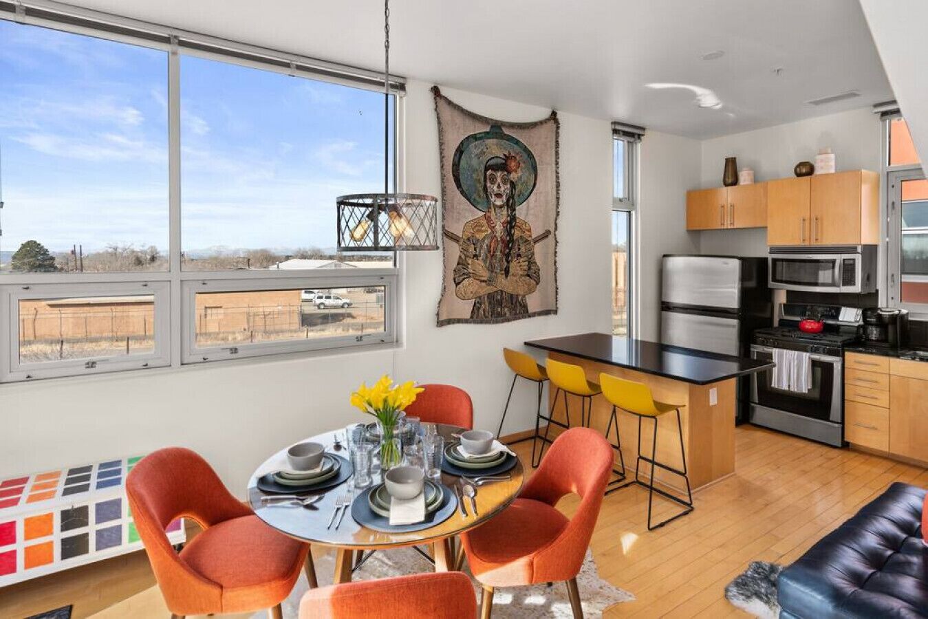 A modern kitchen with a dining area, large windows, and a view of the outside.