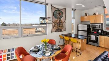 A modern kitchen with a dining area, large windows, and a view of the outside.