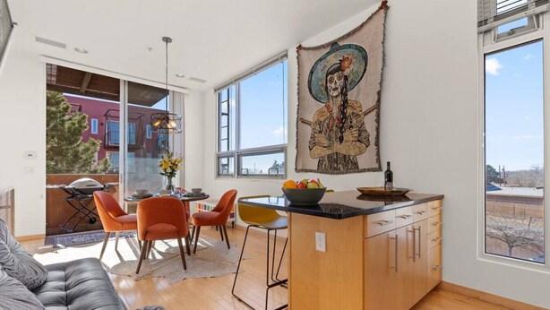 Une cuisine moderne dotée d’un îlot central, de grandes fenêtres et d’un coin repas avec des chaises orange.