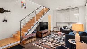 Un salon moderne avec un escalier en bois, un téléviseur à écran plat, un canapé et un tapis à motifs.