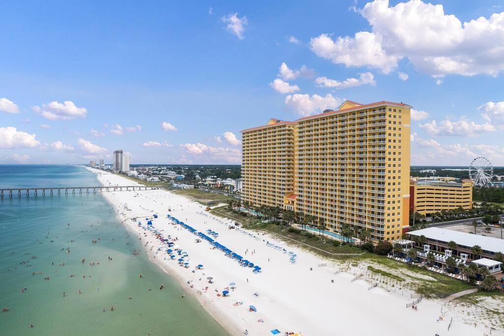 A beachfront hotel with a large building, a pier extending into the ocean, and a Ferris wheel in the background.