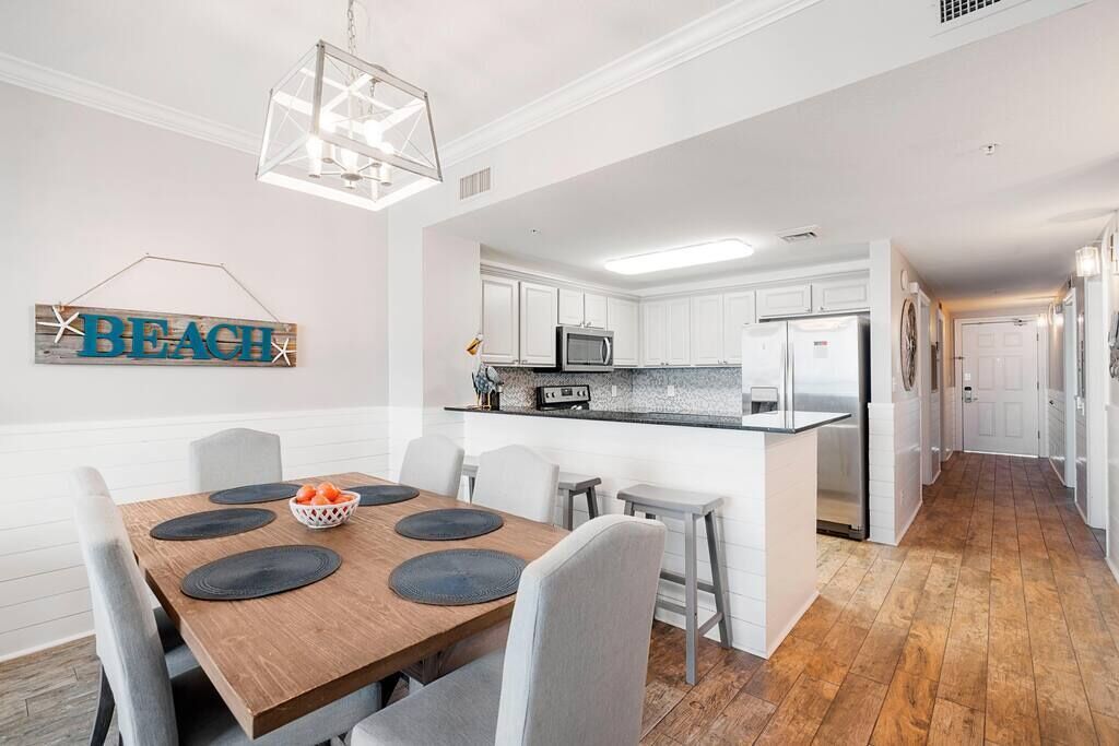 A modern kitchen with white cabinets, a central island, and a dining area with a wooden table and chairs.