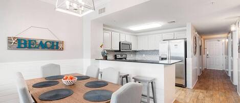 A modern kitchen with white cabinets, a central island, and a dining area with a wooden table and chairs.