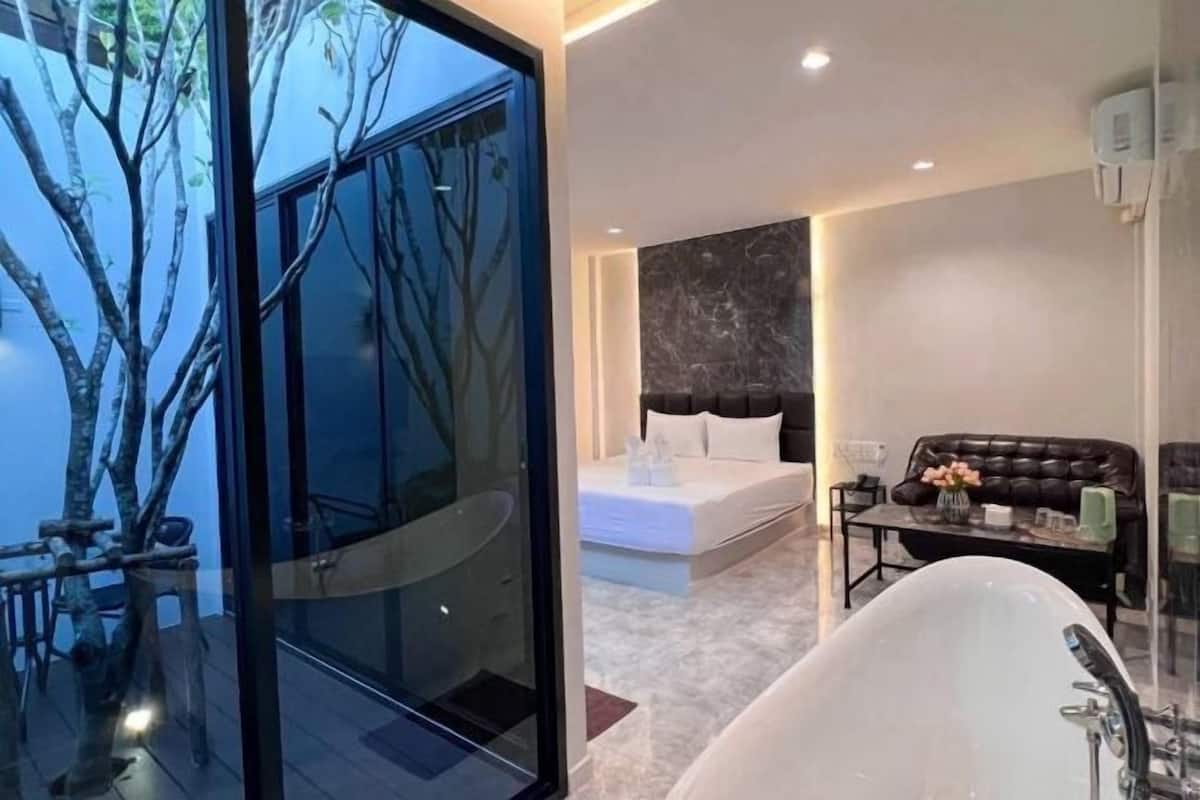 A modern bathroom with a large bathtub, a glass-enclosed shower area, and a bed with a dark headboard.