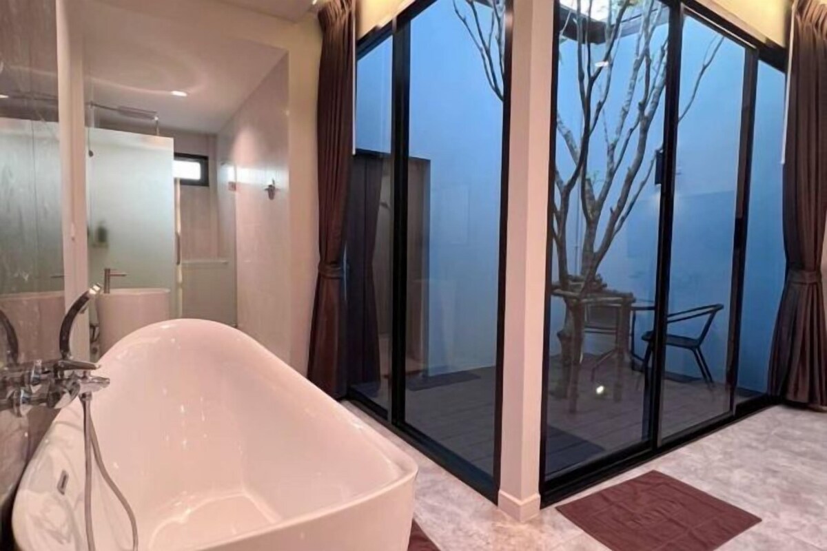 A modern bathroom with a freestanding bathtub, a glass shower enclosure, and a view of an outdoor deck through large sliding glass doors.