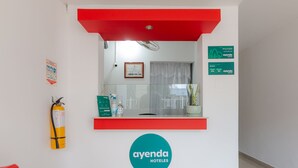 Un comptoir d’accueil surmonté d’une structure rouge, un extincteur et un certificat encadré accroché au mur.