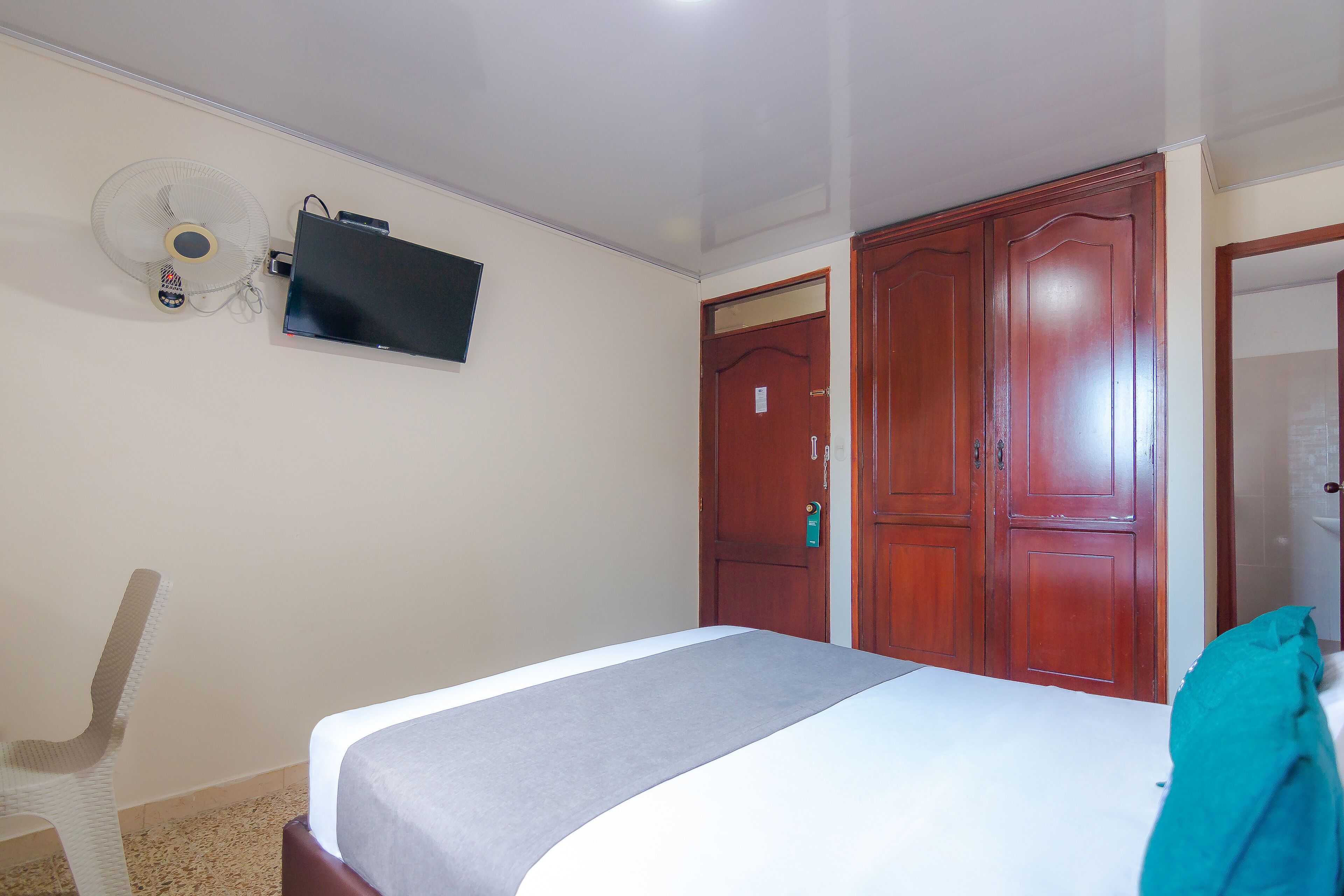 Un dormitorio con cama, televisor montado en la pared, ventilador de techo y armarios de madera.