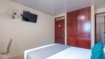 Un dormitorio con cama, televisor montado en la pared, ventilador de techo y armarios de madera.
