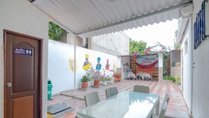 Une terrasse couverte avec une table et des chaises en verre, un panneau indiquant « TOILETTES MIXTES », et un restaurant appelé « Restaurante Jimalta ».