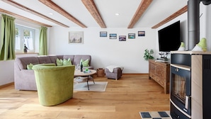 A living room with a sofa, a green ottoman, a fireplace, and a television. - Apartment 'Trendelmühle Lautrach' with Garden & Wi-Fi (Lautrach)
