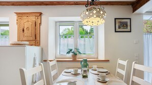 A dining table set with plates, cups, and a kettle, surrounded by white chairs, with a window and a wooden cabinet in the background. - Apartment 'Trendelmühle Lautrach' with Garden & Wi-Fi (Lautrach)