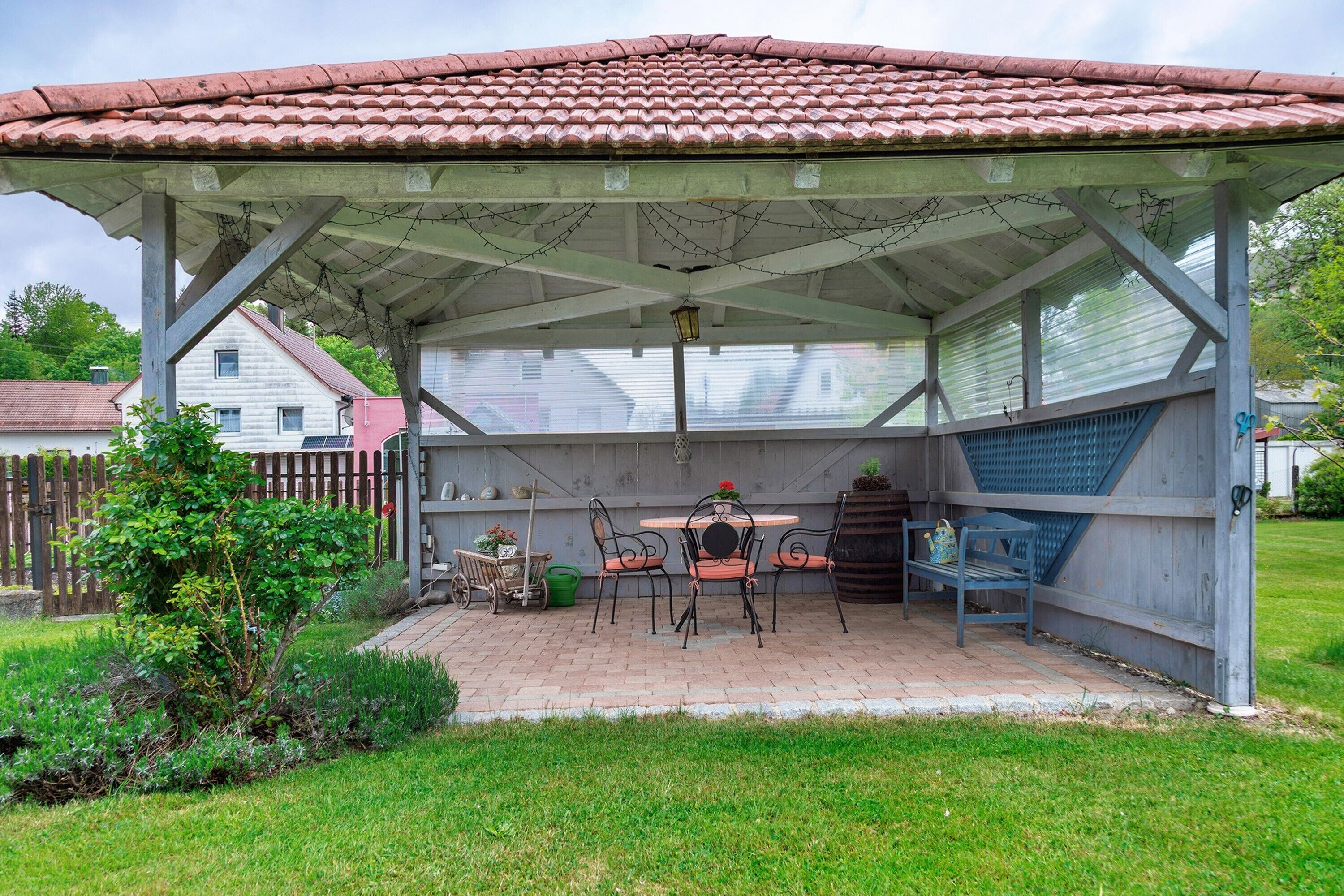 Un patio coperto con tetto in tegole, un tavolo con sedie e un piccolo giardino.