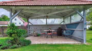 Un patio coperto con tetto in tegole, un tavolo con sedie e un piccolo giardino.