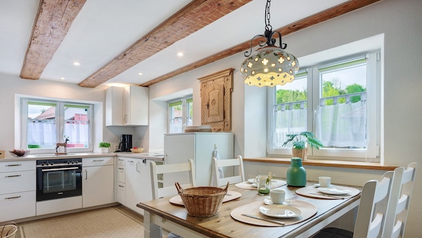 A modern kitchen with white cabinets, a wooden dining table, and a hanging light fixture. - Apartment 'Trendelmühle Lautrach' with Garden & Wi-Fi (Lautrach)