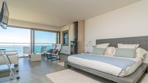 Ein modernes Schlafzimmer mit einem großen Bett, einem Fernseher und Blick auf den Ozean.
