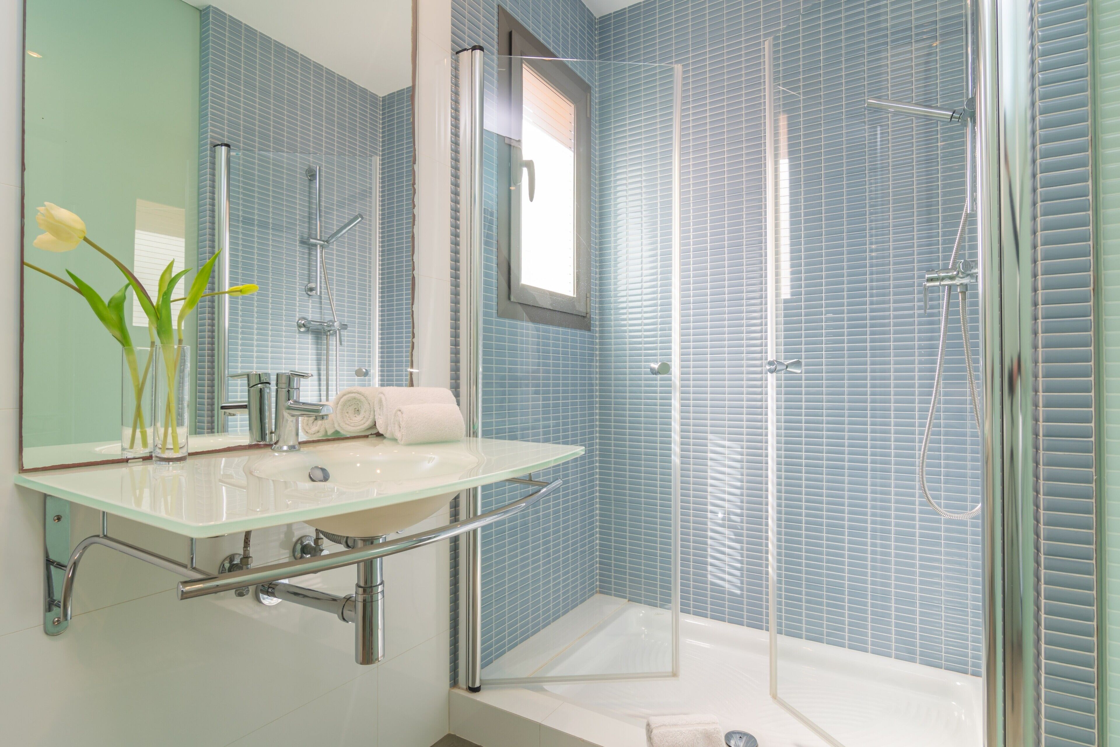 Een moderne badkamer met een douchecabine van glas, een glazen wastafel en een spiegel boven de wastafel.