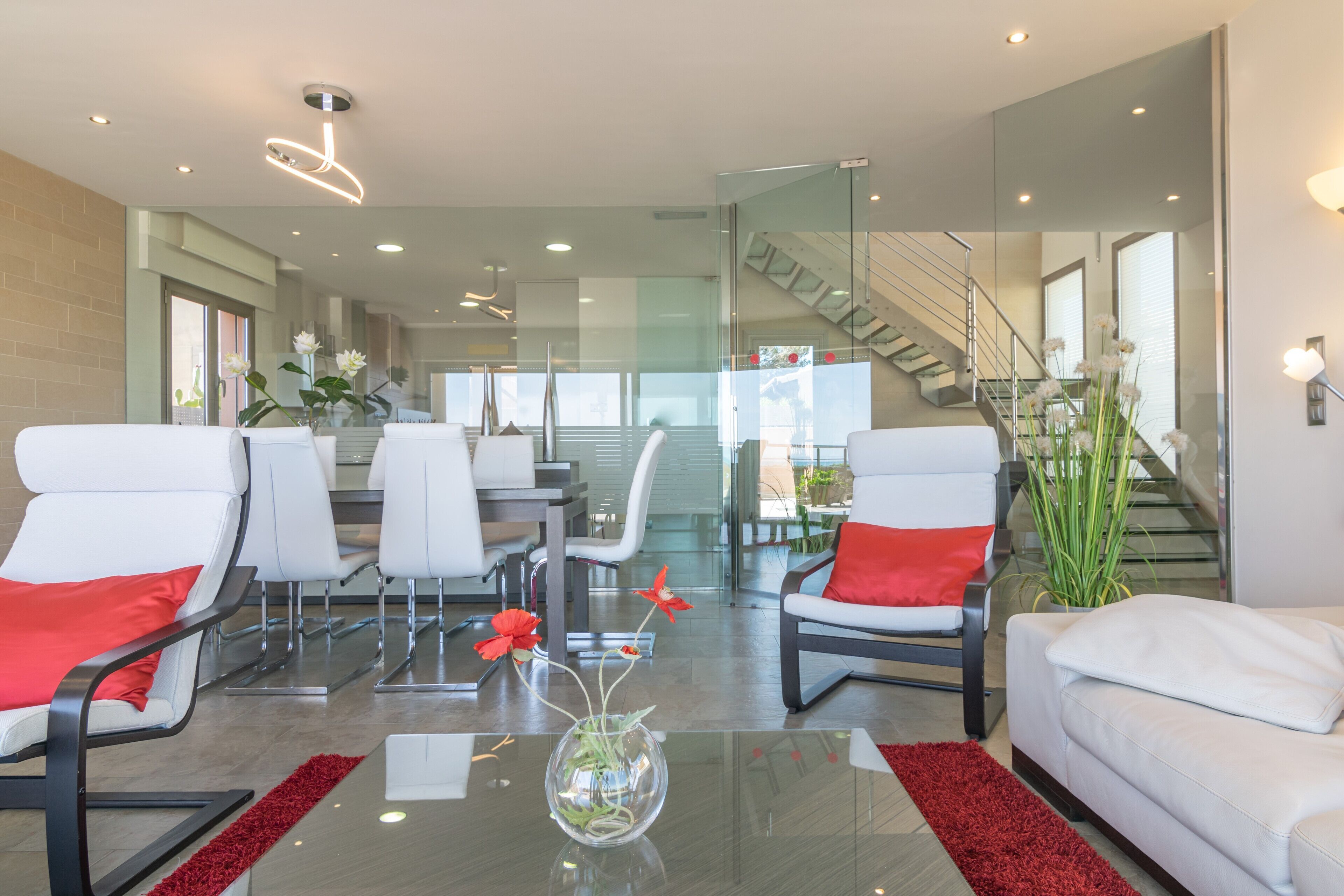 A modern living room with white sofas and chairs, a glass coffee table, and a staircase leading to an upper floor.