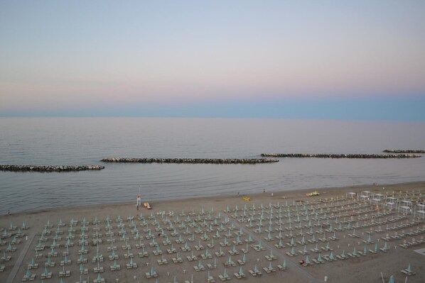 A beach with rows of umbrellas and lounge chairs, a calm sea, and a clear sky.