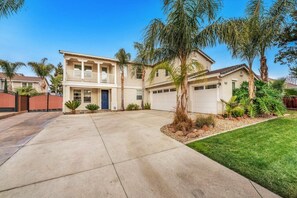 A two-story house with a front driveway, a garage, and a well-maintained lawn with palm trees. - Brentwood Posh 5-Bedroom w/steam shower near hwy (Brentwood)