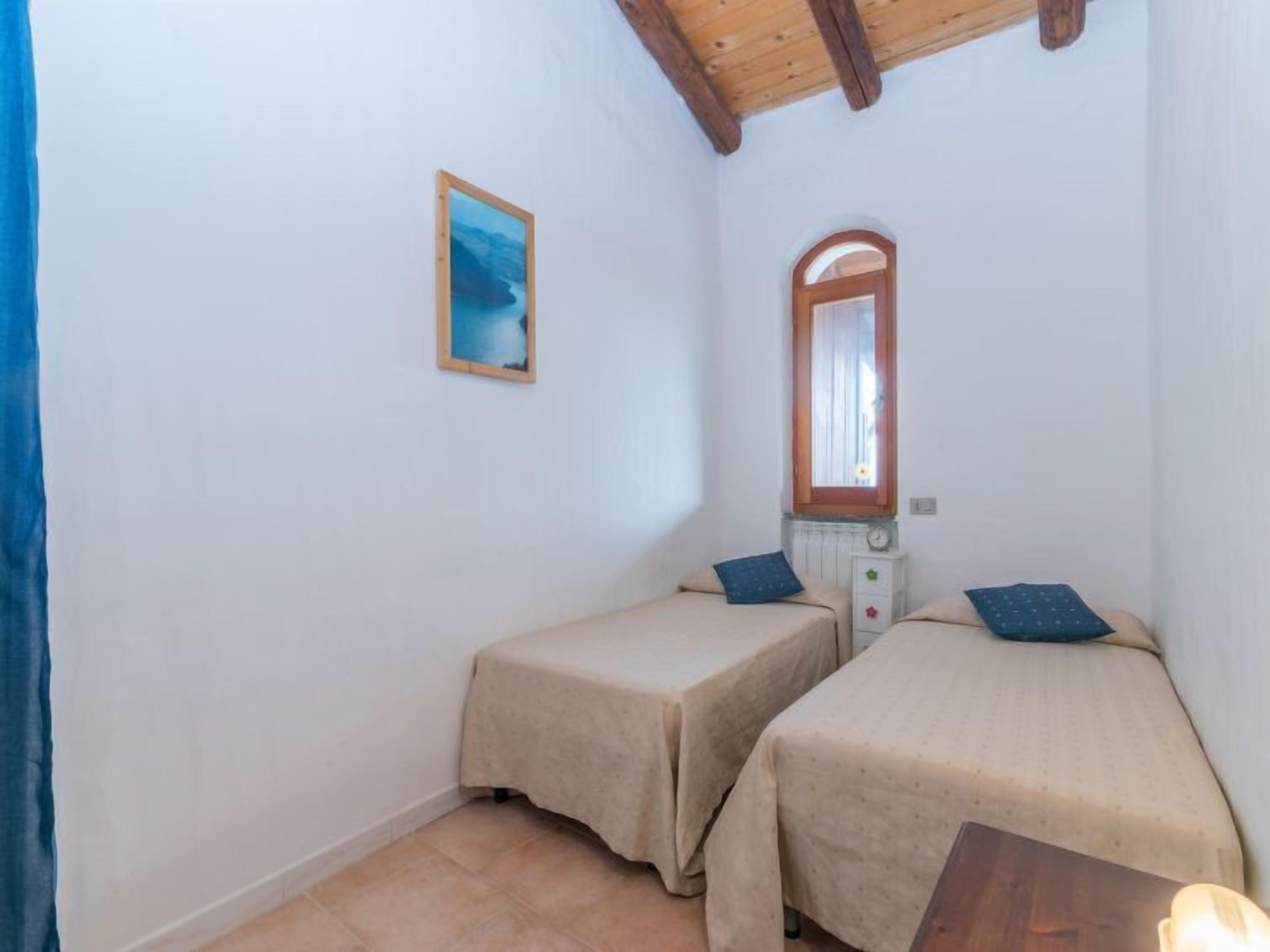 A small, simple room with two single beds, a wooden ceiling, a small table, and a wall-mounted mirror.